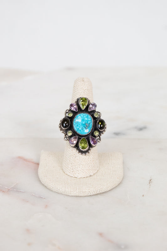 Ring with colorful gemstones on a white stand against a marble background