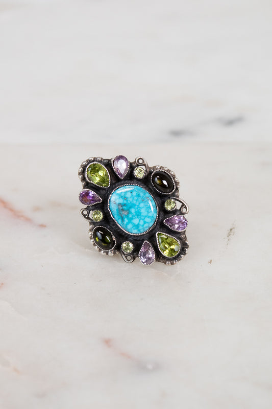 Ring with turquoise stone and multicolored gemstones on a marble background