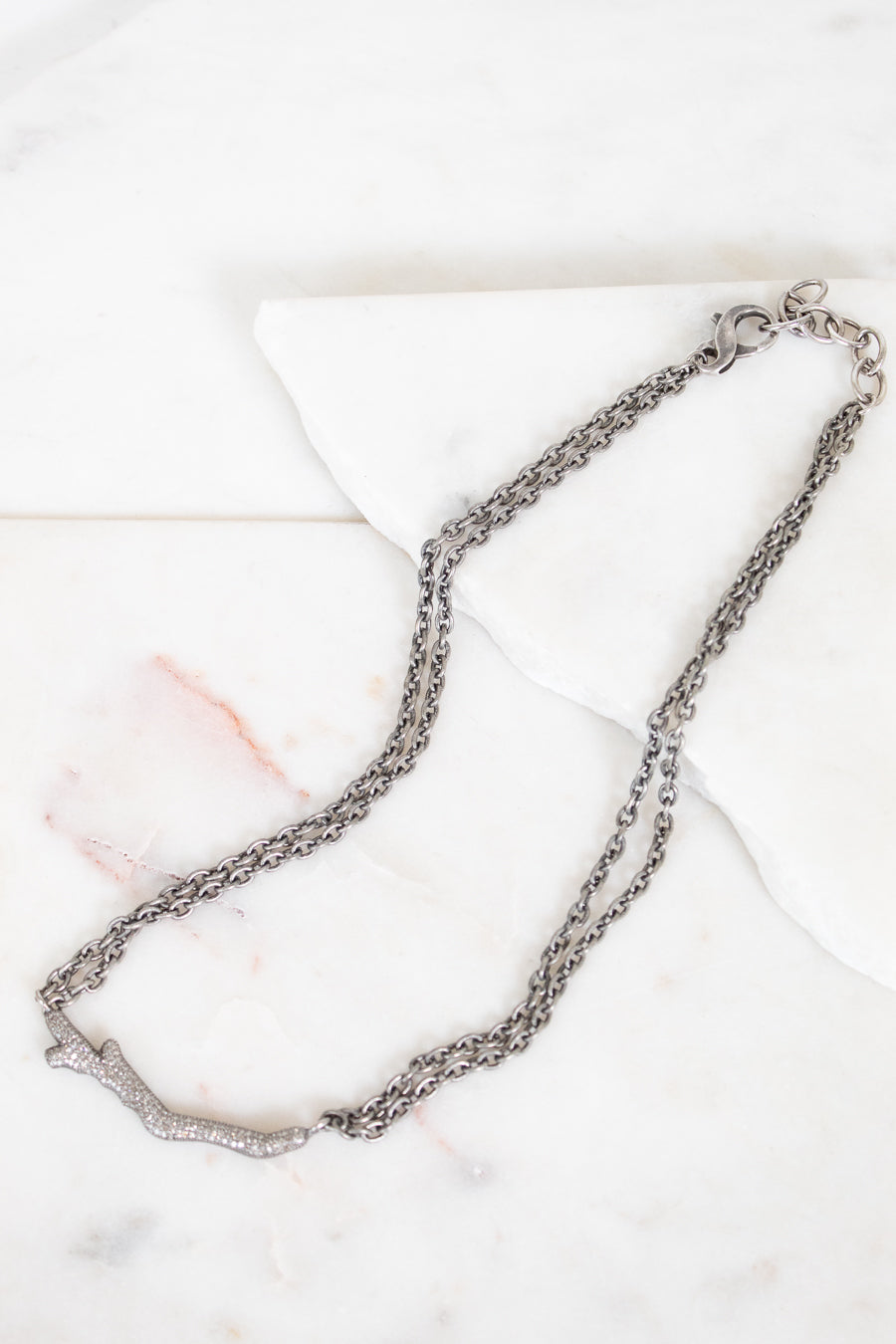 Silver necklace with diamond brand detail on white background