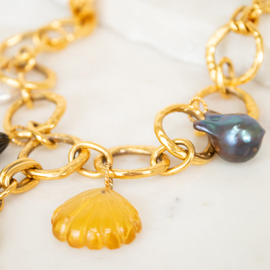 Gold chain necklace with shell and pearl charm on a white surface