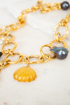 Gold chain necklace with shell and pearl charm on a white surface