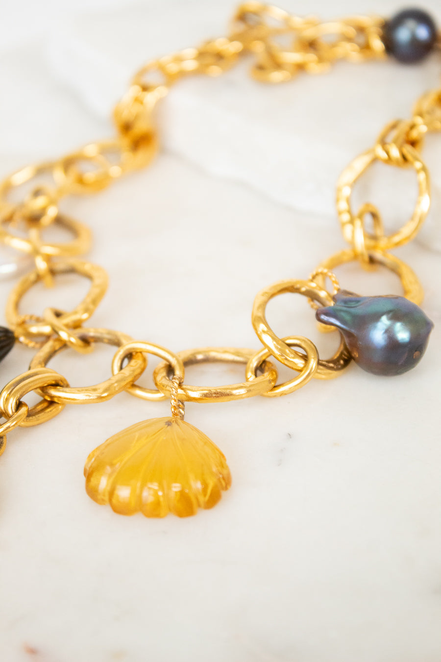 Gold chain necklace with shell and pearl charm on a white surface