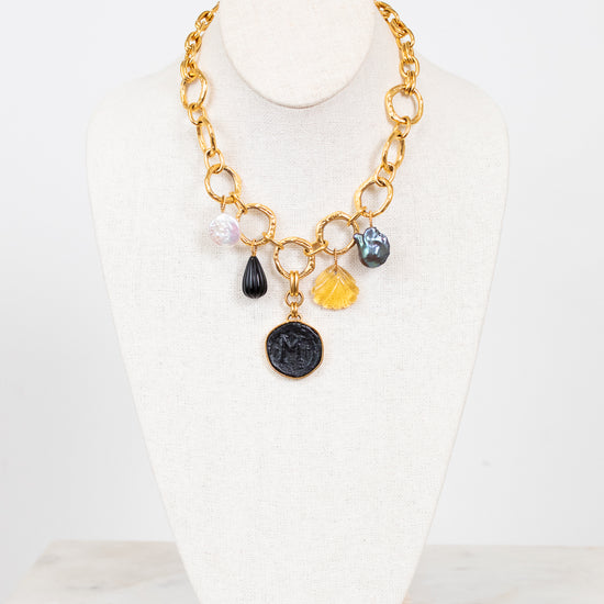 Gold necklace with various colored charms on a white stand