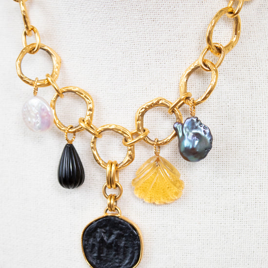Gold chain necklace with various charms on a white background