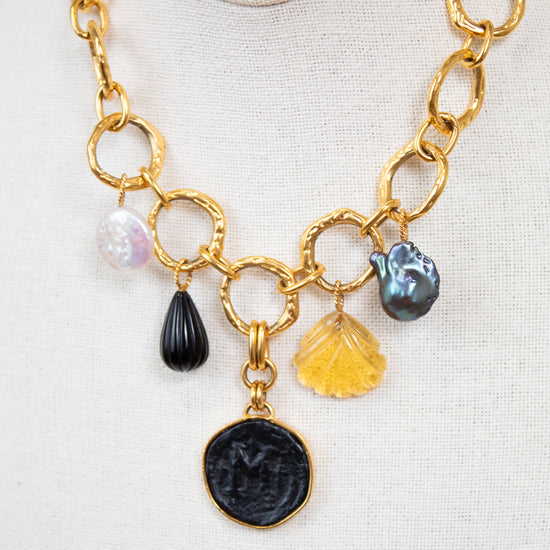 Gold chain necklace with various charms on a white background