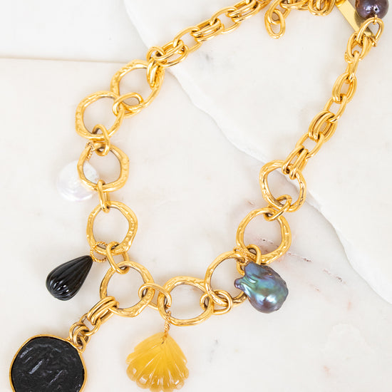 Gold chain necklace with various charms on a marble surface