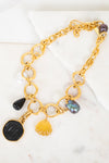 Gold chain necklace with various charms on a marble surface
