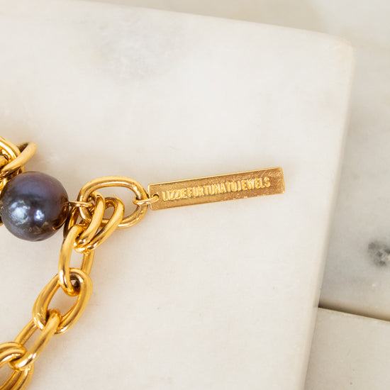 Gold chain bracelet with a pearl on a white surface, featuring the brand name 'Lizzie Fortunato'.