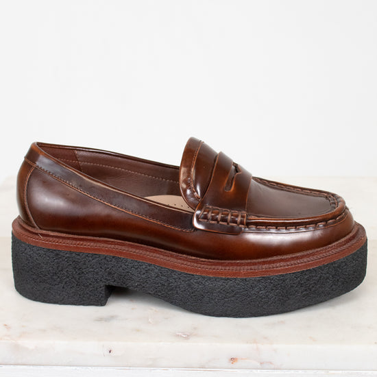 Brown loafer shoe with thick black sole on a light background