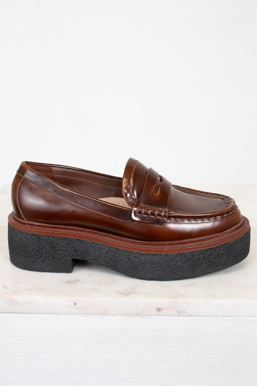 Brown loafer shoe with thick black sole on a light background