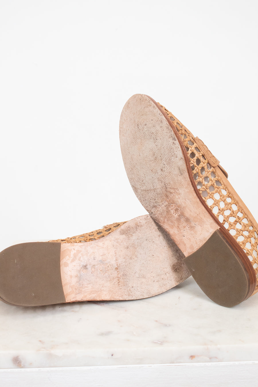 Bottom sole of a pair of flat shoes with woven design on a white marble surface