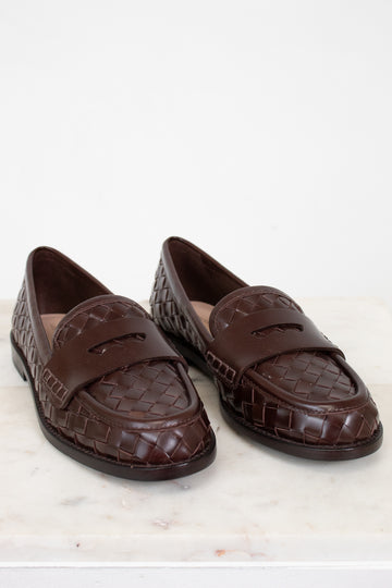 Pair of brown woven loafers on a white marble surface