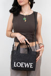 Woman holding a black Loewe handbag against a plain background