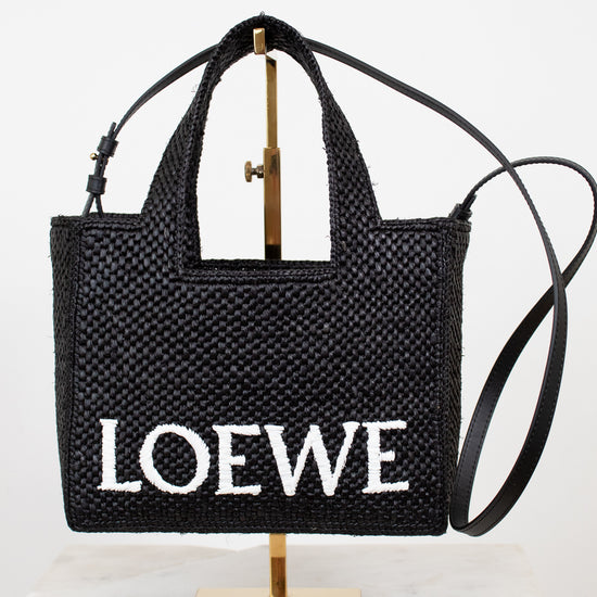 Black woven handbag with 'Loewe' branding on a stand against a white background