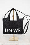 Black woven handbag with 'Loewe' branding on a stand against a white background