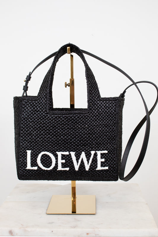 Black woven handbag with 'Loewe' branding on a stand against a white background