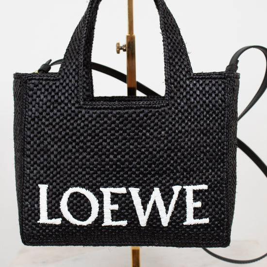Black woven handbag with 'LOEWE' branding on a stand against a white background