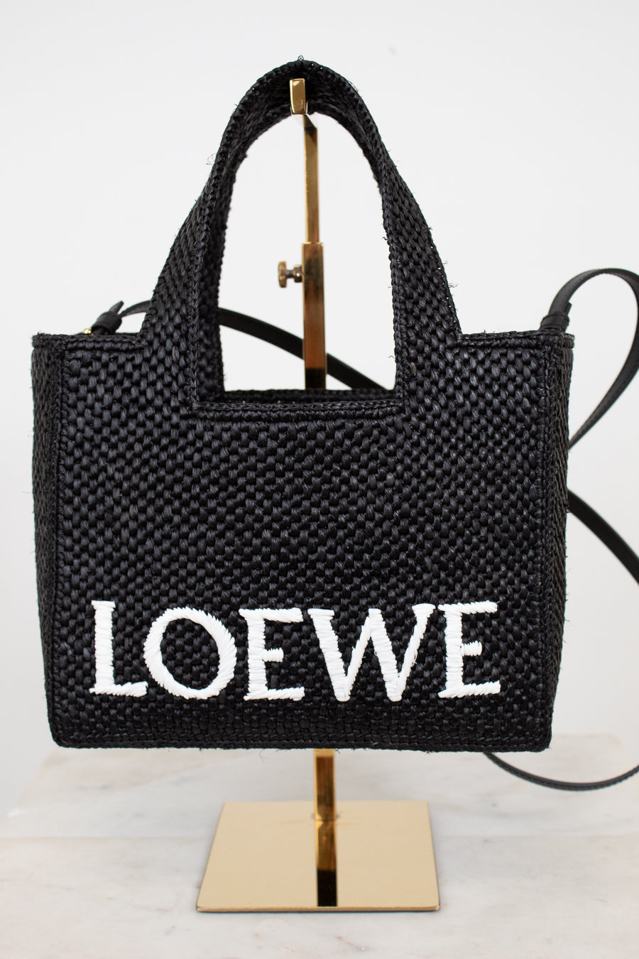 Black woven handbag with 'LOEWE' branding on a stand against a white background