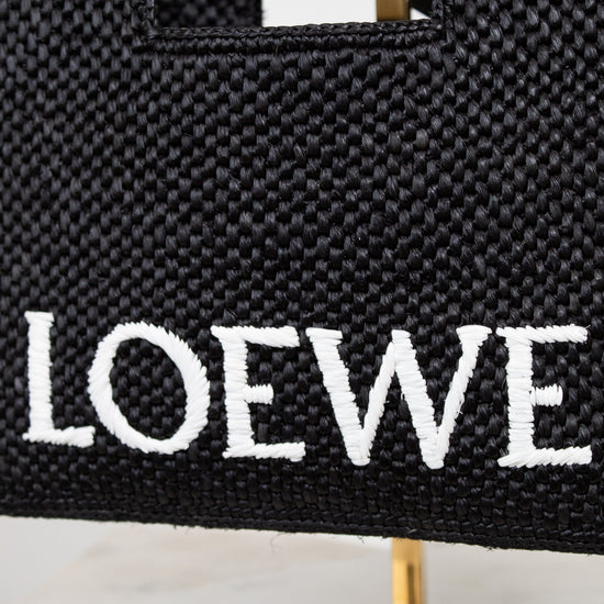Black woven handbag with 'LOEWE' branding on a stand.