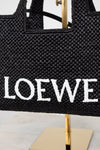 Black woven handbag with 'LOEWE' branding on a stand.