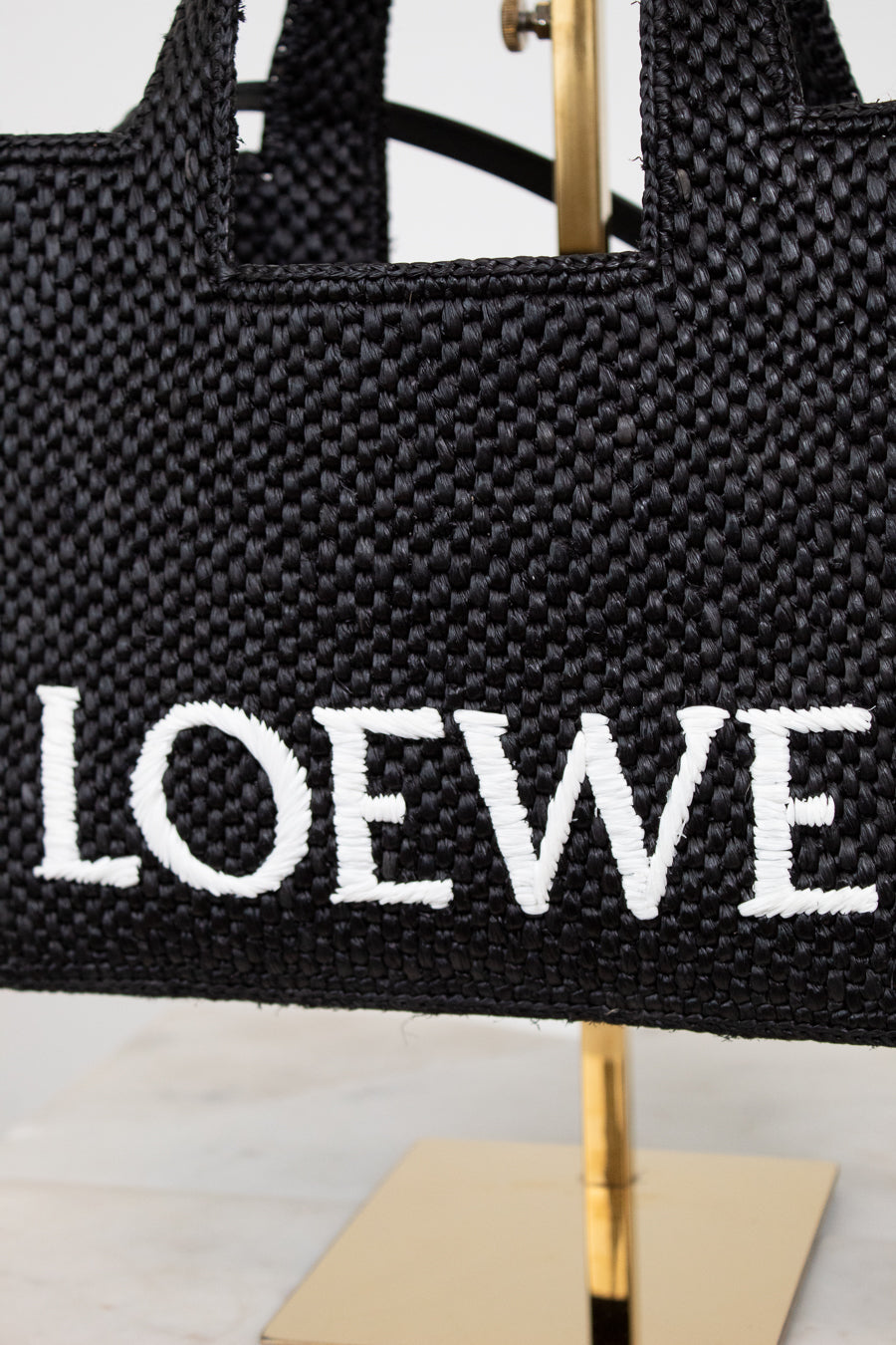 Black woven handbag with 'LOEWE' branding on a stand.