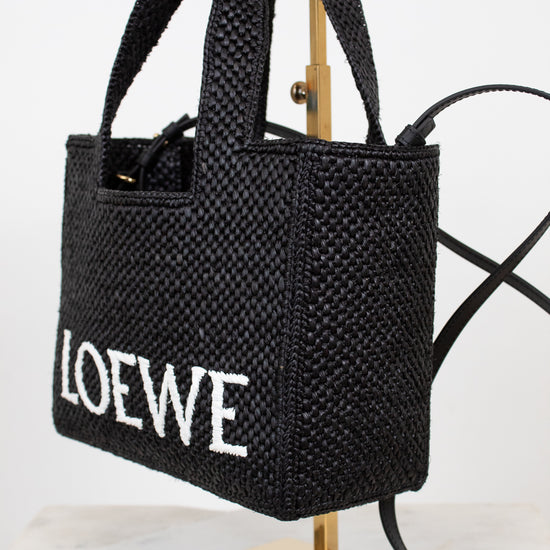 Black woven handbag with 'LOEWE' branding on a stand against a white background