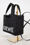 Black woven handbag with 'LOEWE' branding on a stand against a white background