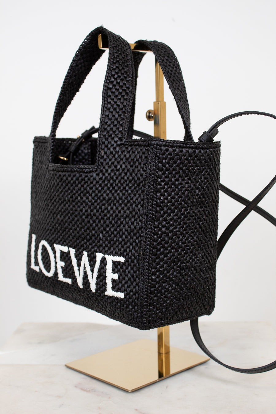 Black woven handbag with 'LOEWE' branding on a stand against a white background
