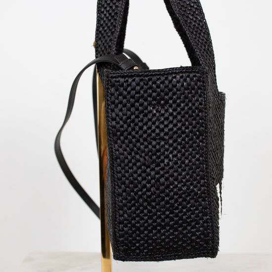 Black woven handbag on a gold stand against a white background