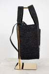 Black woven handbag on a gold stand against a white background