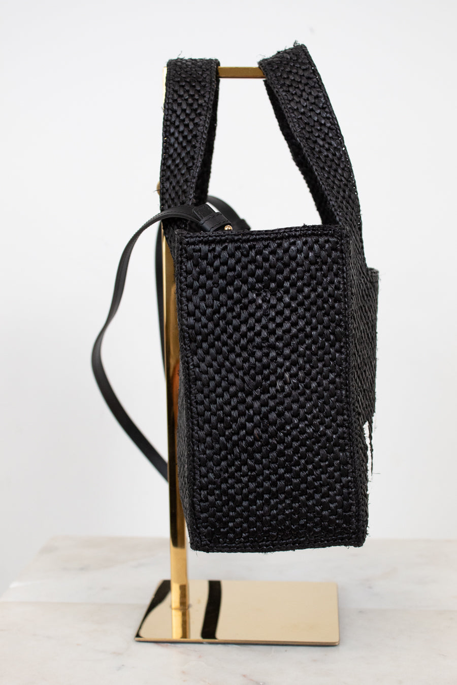 Black woven handbag on a gold stand against a white background