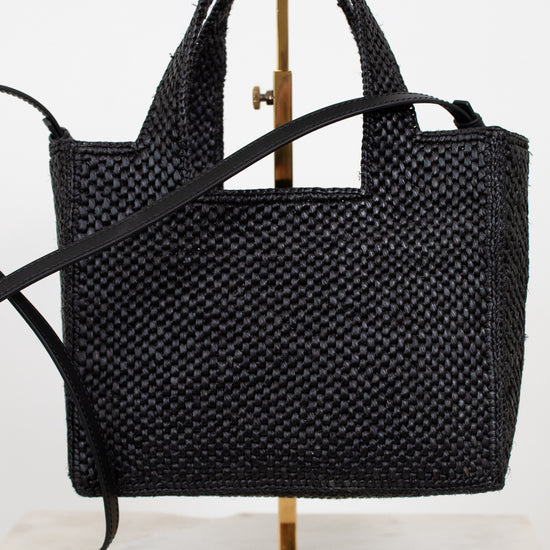 Black woven handbag on a gold stand against a white background