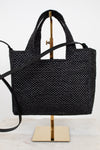 Black woven handbag on a gold stand against a white background