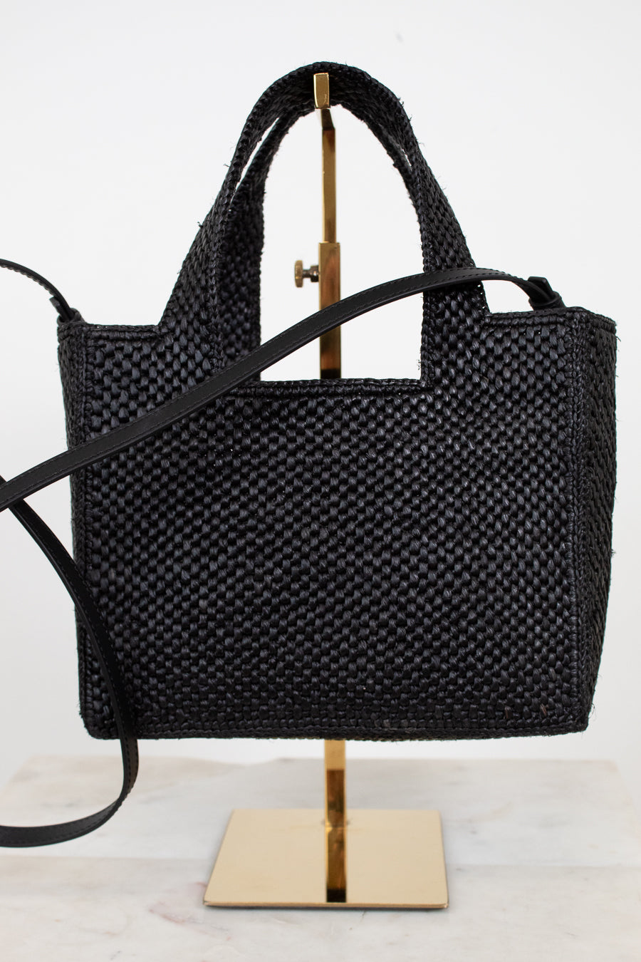 Black woven handbag on a gold stand against a white background