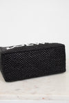 Black woven handbag on a marble surface with a white background