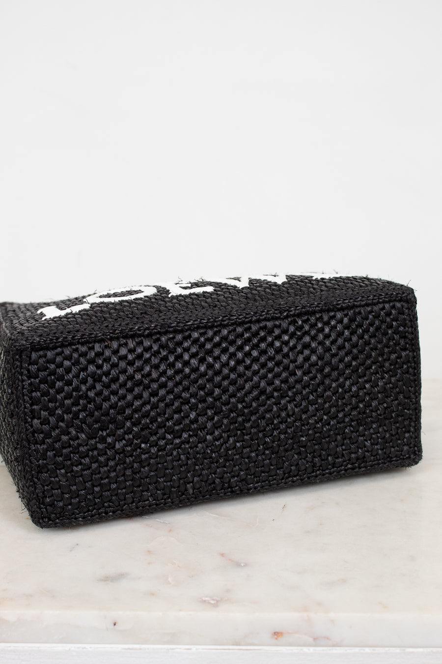 Black woven handbag on a marble surface with a white background