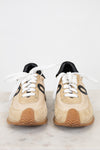 Pair of beige sneakers with black accents on a light gray background