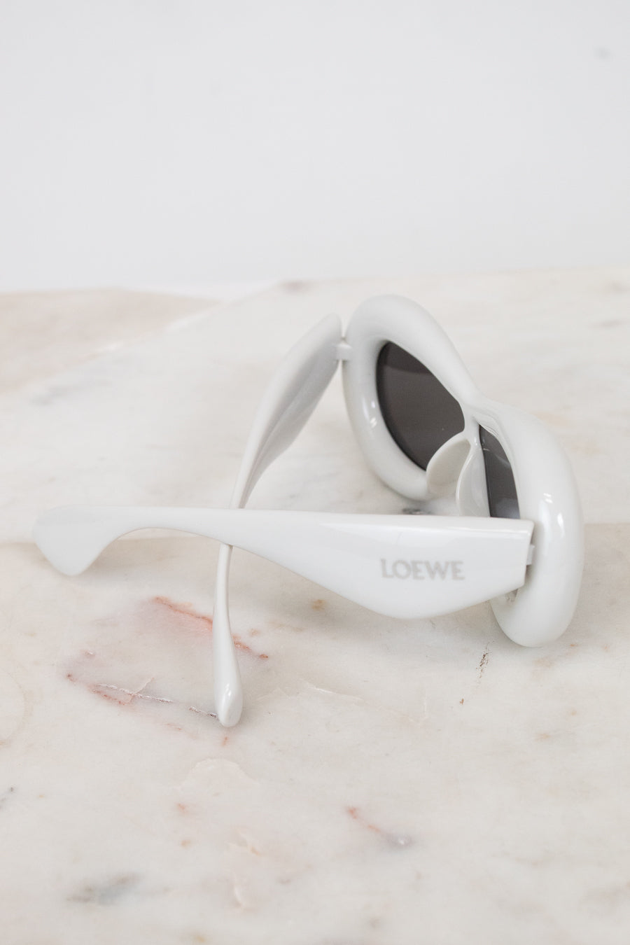 White sunglasses with 'Loewe' branding on a marble surface
