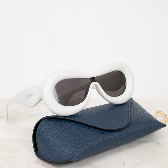 Sunglasses with white frame and dark lenses in a blue case on a light background