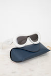 Sunglasses with white frame and dark lenses in a blue case on a light background