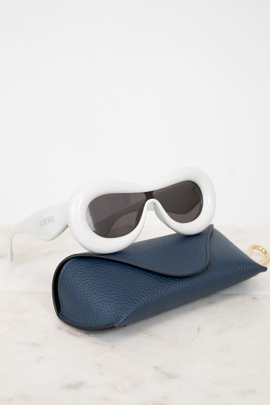 Sunglasses with white frame and dark lenses in a blue case on a light background