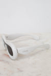 White sunglasses with 'Loewe' branding on a marble surface