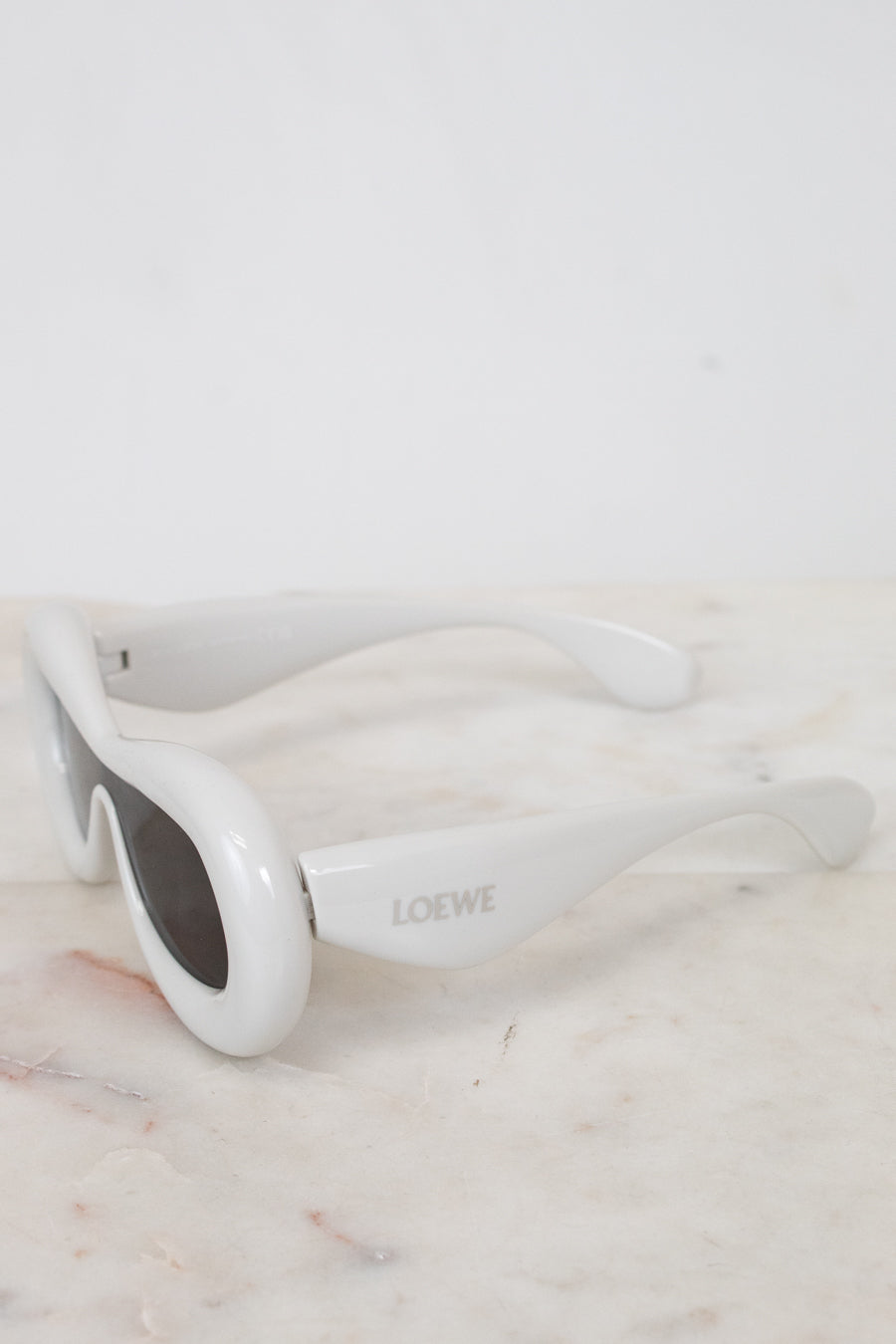 White sunglasses with 'Loewe' branding on a marble surface