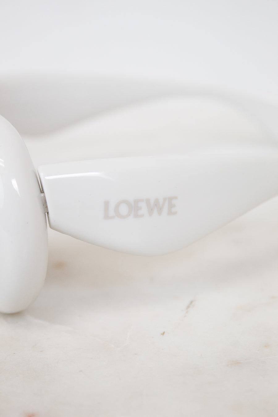 White sunglasses with 'LOEWE' branding on a marble surface