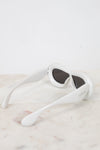 White sunglasses with dark lenses on a light marble surface