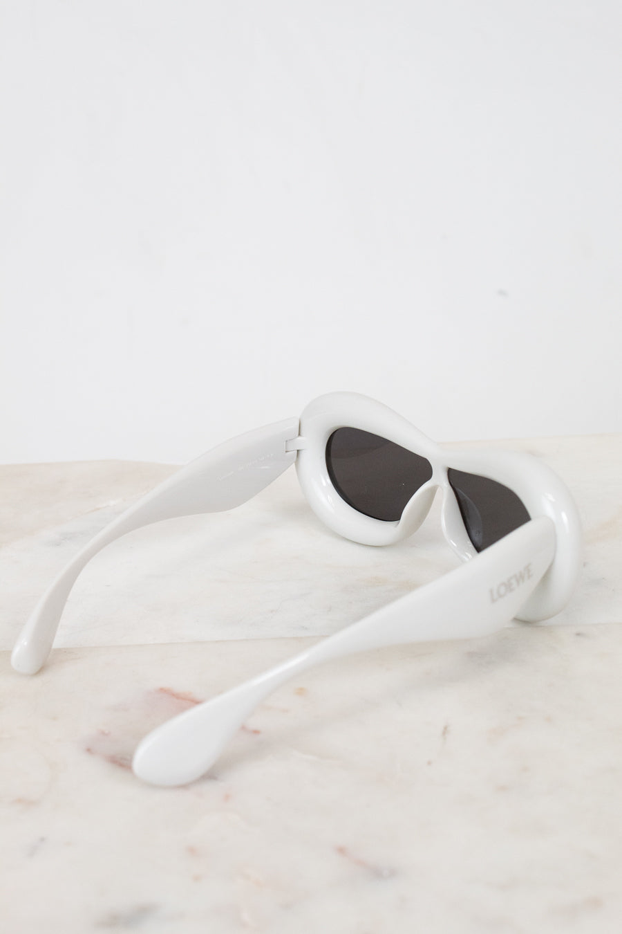 White sunglasses with dark lenses on a light marble surface