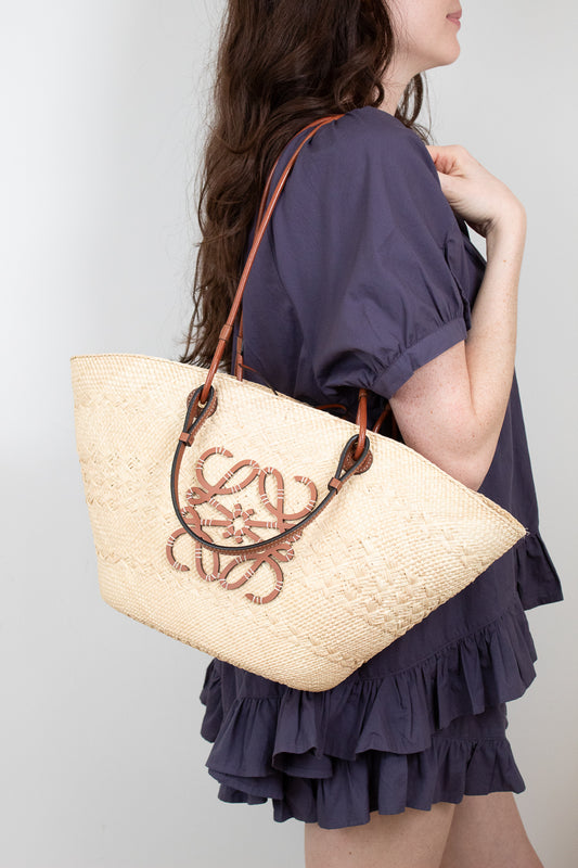 Woman holding a woven tote bag with a brown brand logo against a plain background