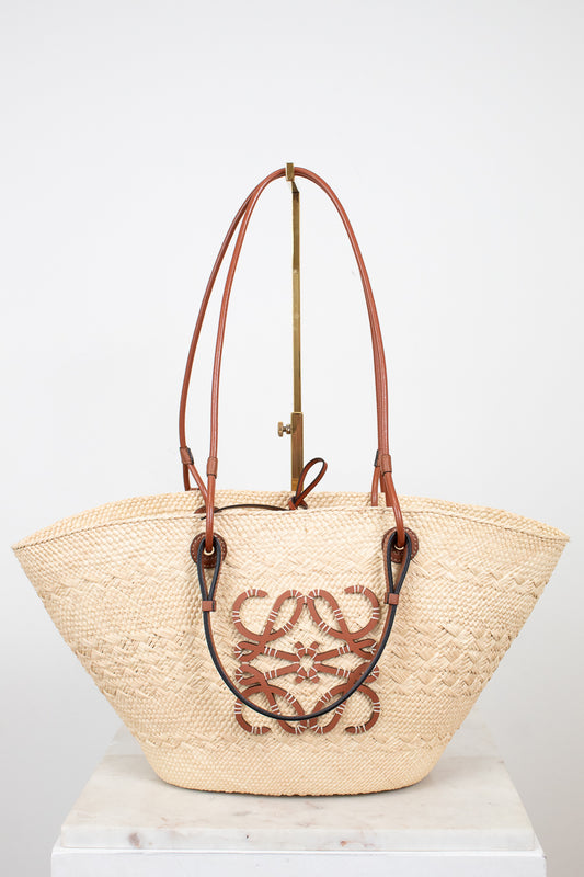 Woven bag with brown handles and brand logo on a white background