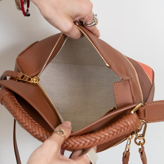 Brown leather handbag with braided handle held by a person against a light background