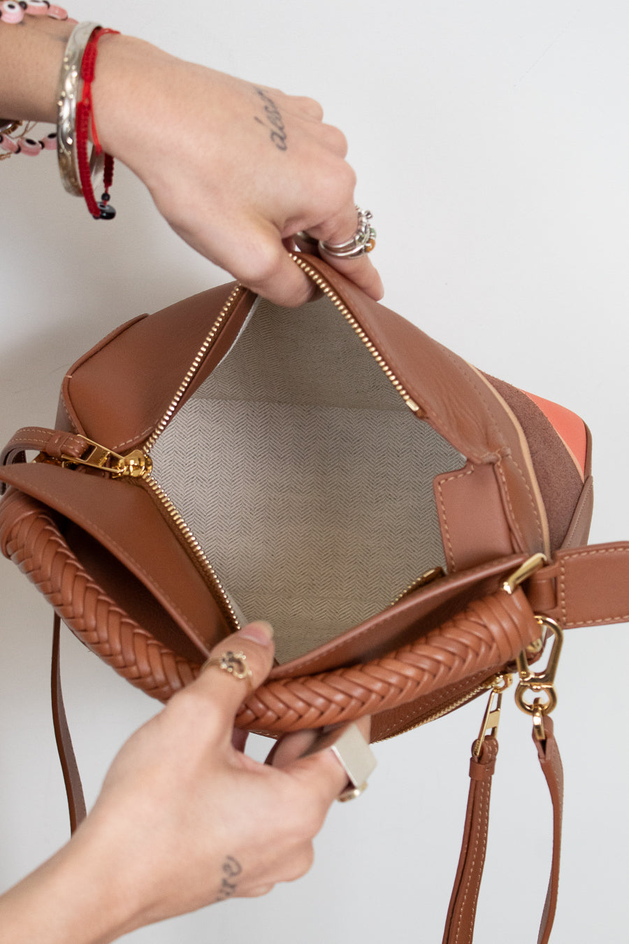 Brown leather handbag with braided handle held by a person against a light background